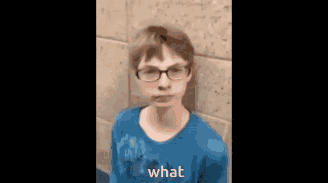 a young boy wearing glasses and a blue shirt is standing in front of a wall .