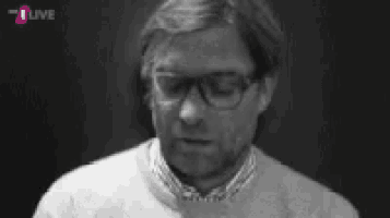 a black and white photo of a man wearing glasses and a sweater that says t live