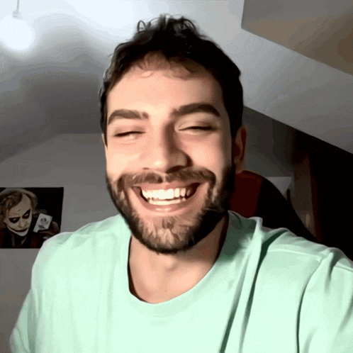 a man with a beard is smiling in front of a joker poster