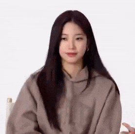 a woman with long black hair is sitting in a chair wearing a brown hoodie .