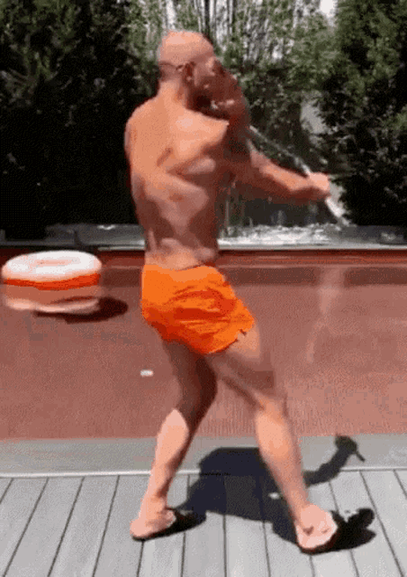 a shirtless man in orange shorts is standing on a deck holding a rope .