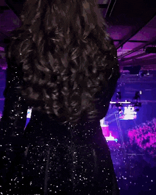 a woman in a black dress is dancing in front of a crowd in a purple room .