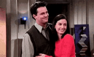 a man and a woman are hugging each other and smiling . the woman is wearing a red sweater .