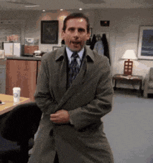 a man in a trench coat and tie is dancing in an office