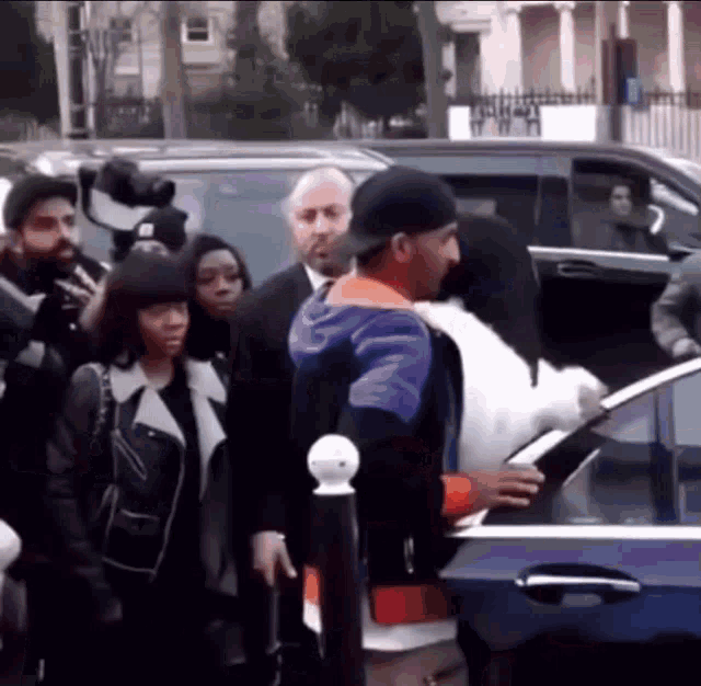 a man in a purple and orange jacket is getting out of a car while a woman looks on .