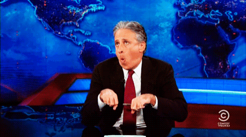 a man in a suit and tie is sitting in front of a screen that says comedy central