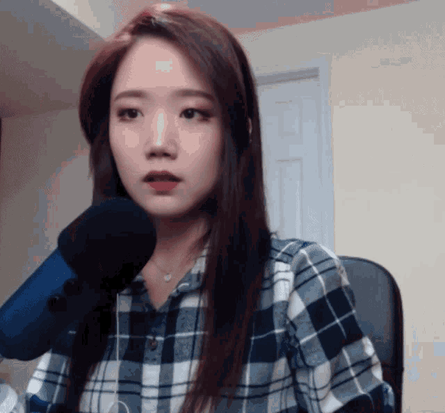 a woman in a plaid shirt is sitting in front of a blue microphone