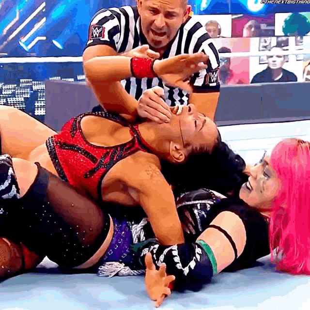 a wrestler with pink hair is laying on the ground while a referee watches