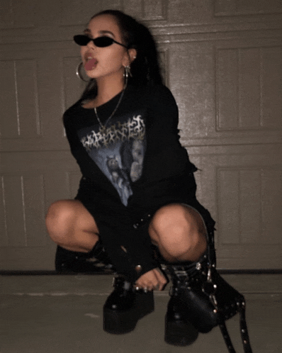 a woman wearing sunglasses and a shirt that says ' apocalypse ' on it is squatting down