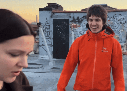a man wearing an orange arcteryx jacket smiles in front of a woman