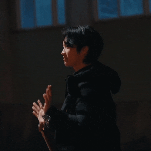 a man in a black jacket holds a guitar in a dark room