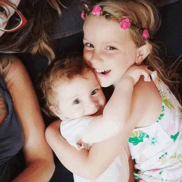 a little girl with a flower crown on her head is hugging another little girl