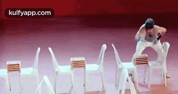 a man is standing on top of a stack of white chairs on a stage .