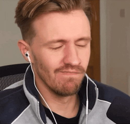 a man with a beard is wearing ear buds and making a funny face
