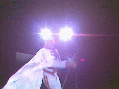 a person in a white robe is standing in front of a microphone with purple lights behind them