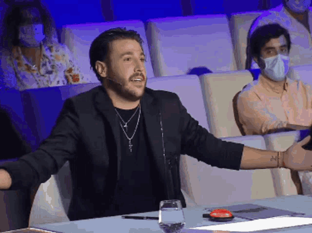 a man in a black jacket is sitting at a table with his arm outstretched