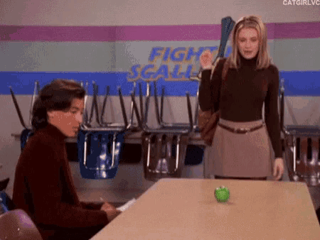 a man is sitting at a table with an apple on it and a woman is standing next to him .