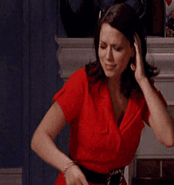 a woman in a red shirt is standing in front of a fireplace holding her head
