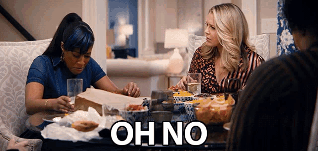 two women sit at a table with a sign that says oh no on it