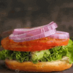a close up of a sandwich with lettuce , tomato , and onions on a bun on a table .