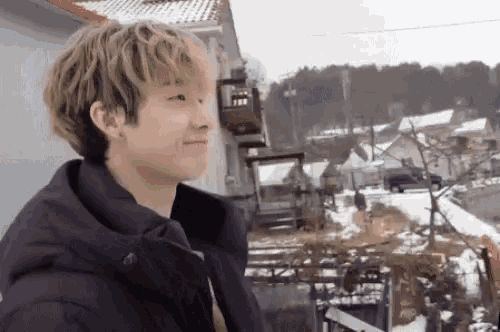a young man in a black jacket is standing in the snow in front of a house .