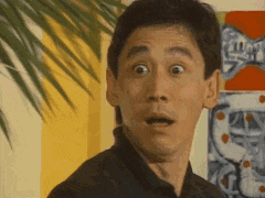 a man is making a surprised face while standing in front of a palm tree .