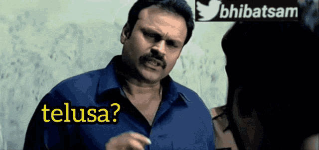 a man in a blue shirt is talking to another man and the words telusa are on the screen