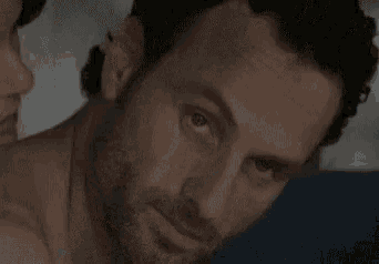 a close up of a man 's face with a beard and a woman in the background .