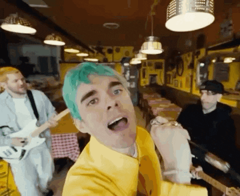 a man with green hair is singing into a microphone while two other men play guitars .