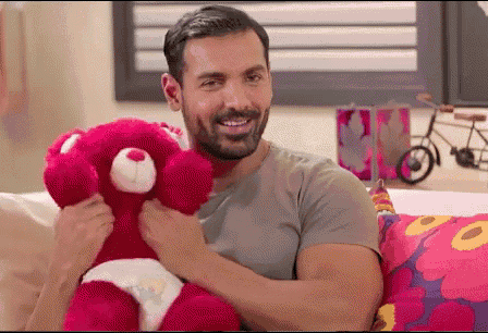 a man is holding a pink teddy bear with a diaper on