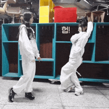 two girls are dancing in front of a shelf with chinese writing
