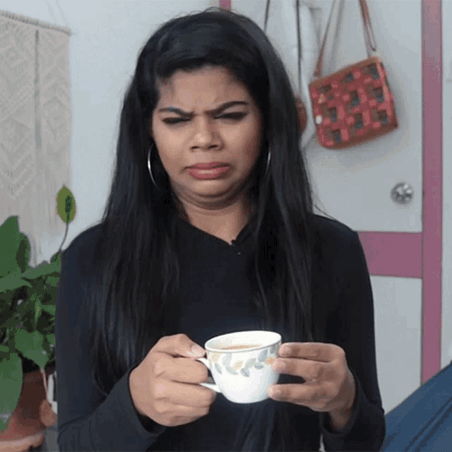 a woman holding a cup of tea making a funny face
