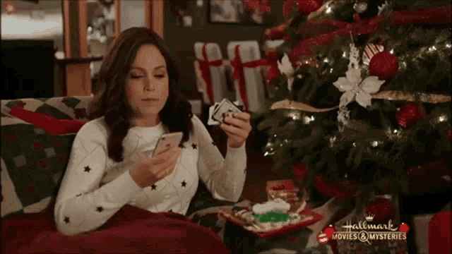 a woman is sitting on a couch looking at her phone and holding a deck of cards