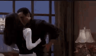 a man and woman are kissing in front of a window in a living room .