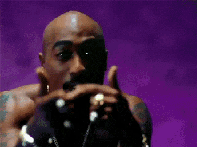 a bald man is holding a microphone in front of a purple background ..