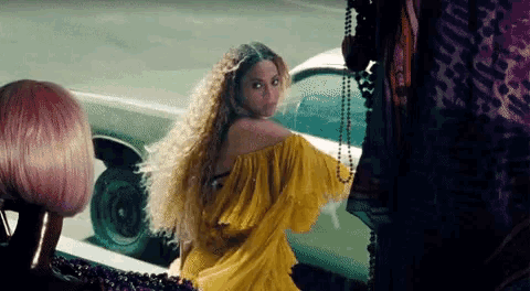 a woman in a yellow dress is standing next to a car and a woman in a pink wig .