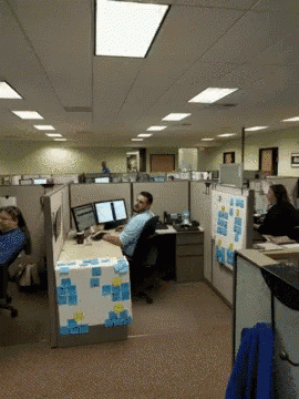 a man sits at a desk in an office cubicle with sticky notes on it