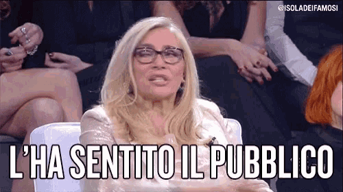 a woman wearing glasses says l ' ha sentito il pubblico in front of a group of people