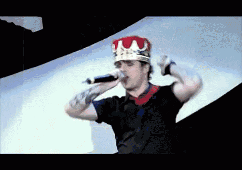 a man wearing a crown holds a microphone in his mouth