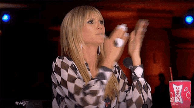 a woman is clapping her hands in front of a microphone while holding a sonic cup