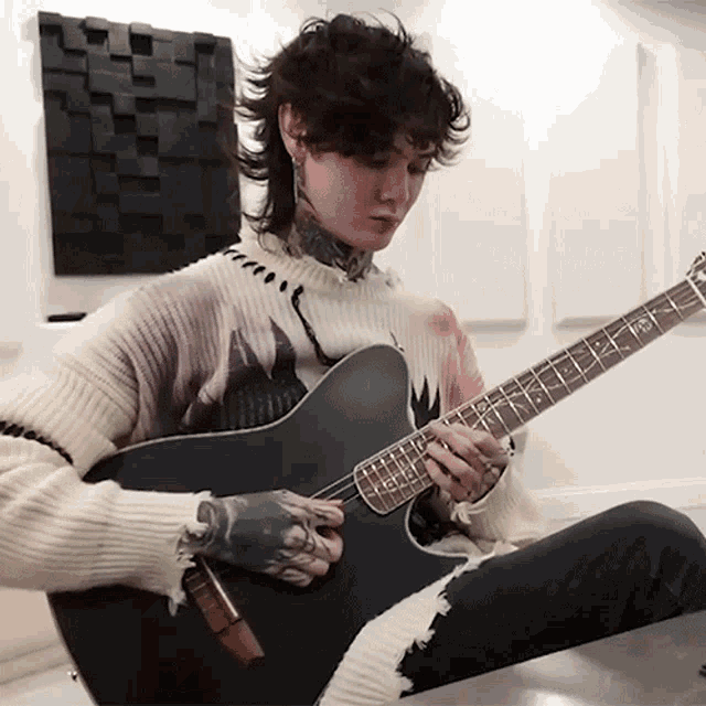 a man in a sweater is playing a guitar with the letter z on the neck