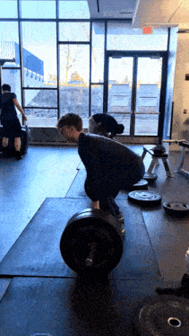 a man is lifting a barbell in a gym with a sign that says ' exit ' on it