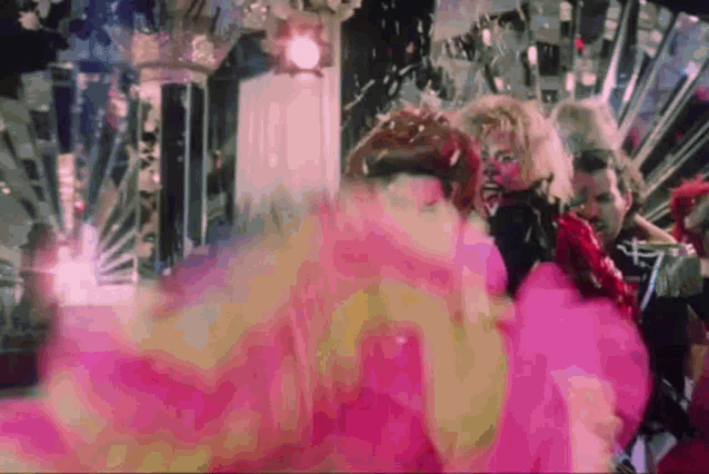 a woman in a pink dress is dancing in a room with other people .