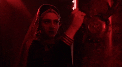 a woman in a veil is standing in a dark room with red lights .