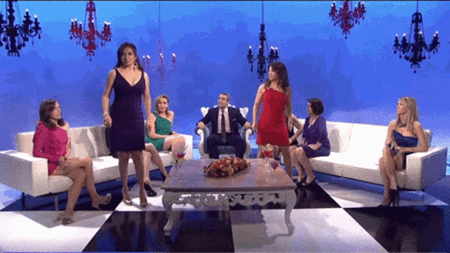 a woman in a purple dress stands in front of a group of women sitting on couches