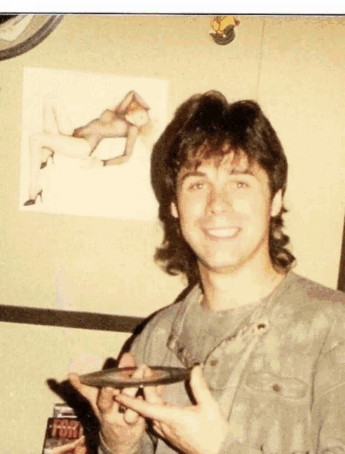 a man is holding a cd in front of a poster that says " tom "