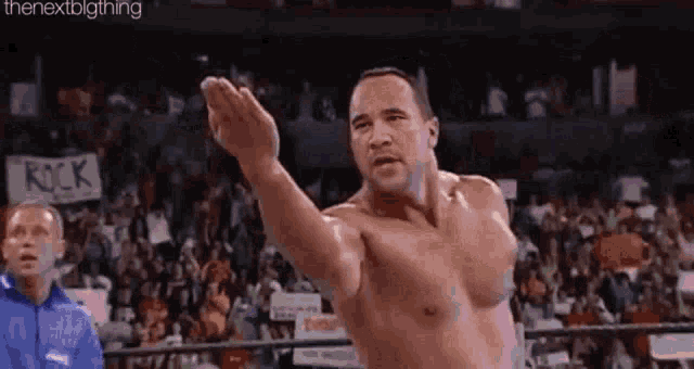 a shirtless wrestler is standing in a wrestling ring with his arms outstretched .