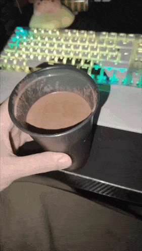 a person is holding a cup of chocolate sauce in front of a keyboard
