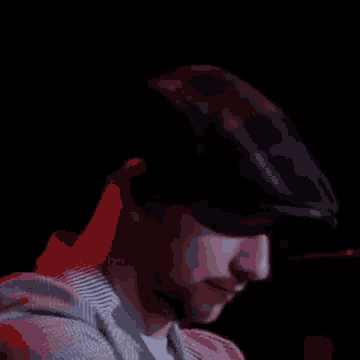 a man wearing a hat and ear buds looks at the camera in a dark room .