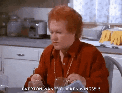 a woman with red hair is sitting in a kitchen eating chicken wings and saying everton wants chicken wings !!!